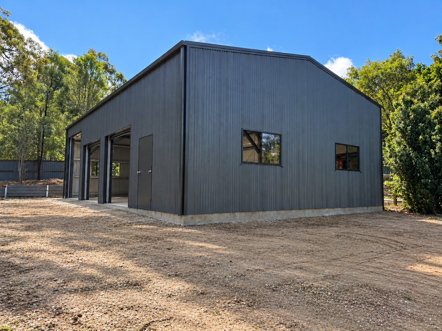 Corner view of a dark Colorbond gable shed with open roller doors, Beaudesert